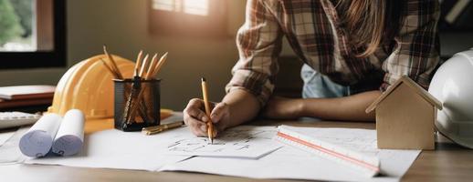 junge ingenieure, die einen roten stift halten, der auf ein gebäude auf einem plan zeigt, und mit einem computer-laptop eine präsentation für das treffen auf der arbeitsstelle schreiben. foto