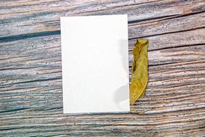 a5-papiergrußkartenmodell mit trockenen blättern auf holzhintergrund foto