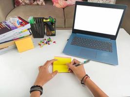 Mockup-Bild, Laptop-Computer mit leerem Bildschirm mit einer Frau, die Notizen auf gelbem Papier mit Stift im modernen Wohnzimmer macht. Laptop-Modelle foto