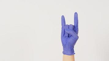 Hand trägt violetten oder lila Handschuh und macht Rock-Handzeichen auf weißem Hintergrund. foto