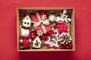 handgemachtes pflegepaket, saisonale geschenkbox mit spielzeug, weihnachtsdekor auf rotem tisch personalisierter umweltfreundlicher korb für familie, freunde, mädchen für den 24. dezember, weihnachten, neujahrstag flach gelegt. foto