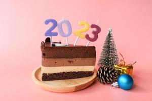 Schokoladenkuchen mit Zahlen 2023 und Zubehör für Weihnachten und Neujahr isoliert auf rosa Hintergrund. foto