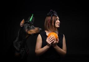 Porträt eines Dobermann-Hundes mit einem Mädchenbesitzer. in Faschingskostümen mit Kürbis. foto
