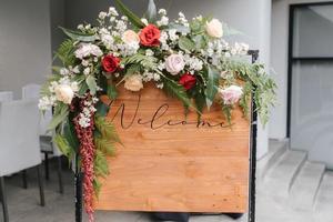 Ein Willkommensschild mit einer schönen Blumendekoration, das vor dem Hochzeitseingang steht. foto
