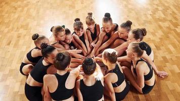 im Kreis sitzen. Gruppe weiblicher Kinder, die gemeinsam Sportübungen im Innenbereich praktizieren foto