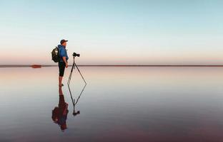 fotograf in lässiger kleidung arbeitet mit der kamera und macht eine aufnahme des wunderschönen meeres foto