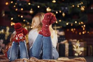 mutter mit ihrer kleinen tochter, die sich an den weihnachtsferien in festlicher kleidung drinnen auf den boden legt foto