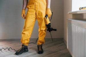 Handwerker in gelber Uniform mit drinnen stehendem Bohrer. haussanierungskonzept foto