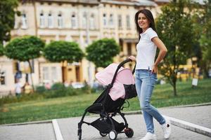 mit rosa kinderwagen. hübsche junge frau hat tagsüber ein wochenende in der stadt foto