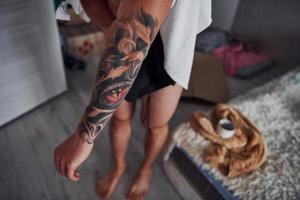Der Typ zeigt sein Tattoo auf dem Arm zu Hause nach der Dusche foto