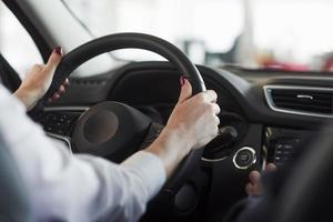 Hände am Lenkrad. frau in offizieller kleidung, die ihr neues auto im autosalon probiert foto