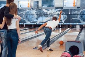 Paar umarmt sich hinter dem Mann. Junge, fröhliche Freunde haben an ihren Wochenenden Spaß im Bowlingclub foto