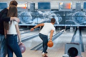 orangefarbene Kugel. Junge, fröhliche Freunde haben an ihren Wochenenden Spaß im Bowlingclub foto