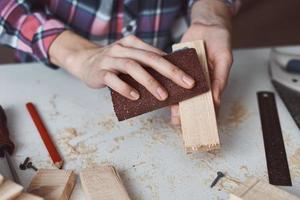 Tischlerhände polieren Holzbohlen mit Sandpapier foto