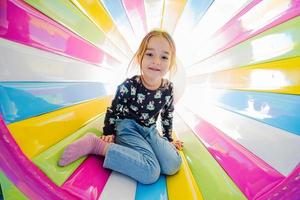 lustiges Mädchen, das auf dem Spielplatz im Indoor-Spielzentrum in farbiger Röhre spielt. foto