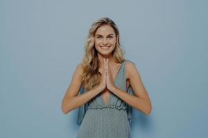 hoffnungsvolles blondes Mädchen, das ihre Hände in betender Geste zusammenhält foto