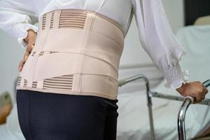 asiatische Patientin mit Rückenschmerzen-Unterstützungsgurt für orthopädische Lendenwirbelsäule mit Gehhilfe. foto