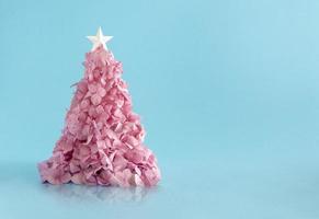 Weihnachtsbaum aus kleinen rosa Blumen vor hellblauem Hintergrund. minimale Flat-Lay-Komposition. foto