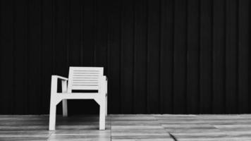Holzstuhl auf braunem Fliesenboden mit schwarzer Rollladenwand für Hintergrund und Kopierfläche rechts. Objekt zum Platz nehmen mit dunkler Edelstahltapete in monochromem Ton. foto