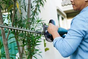 Gärtner trimmt Busch mit elektrischen Heckenscheren im Garten. Hobby zu Hause. foto