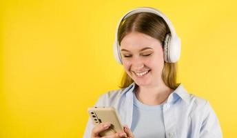 Nahaufnahmeporträt des jungen glücklichen Studenten in den Kopfhörern unter Verwendung des Smartphones. Anwendung für Sprachen. Hören Sie Podcasts, Musik. Verwenden Sie soziale Medien Studioporträt. zurück zur Schule foto