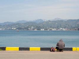 Fischer auf dem Pier an der Küste. Ein Mann sitzt mit einer Angelrute am Strand. foto