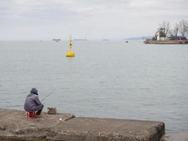 Fischer auf dem Pier an der Küste. Ein Mann sitzt mit einer Angelrute am Strand. foto
