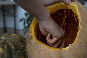 Frau, die großen orangefarbenen Kürbis für Halloween schnitzt, während sie zu Hause am Holztisch sitzt foto