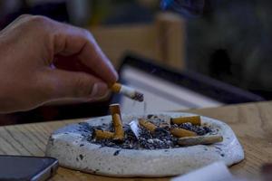 junger mann, der auf einem holztisch raucht, aschenbecher mit mehreren gebrauchten zigarren, mexiko foto