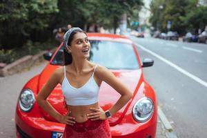 Porträt einer hübschen kaukasischen Frau, die gegen ein neues rotes Auto steht foto