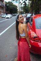 Porträt einer hübschen kaukasischen Frau, die gegen ein neues rotes Auto steht foto