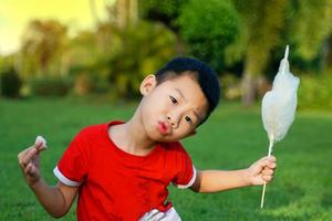 asiatischer junge, der zuckerwatte genüsslich isst. Zuckerwatte wird aus Zucker hergestellt, der in dünne Streifen gesponnen wird. wie eine Wolke, viele Farben je nach Farbe. weicher und selektiver Fokus. foto