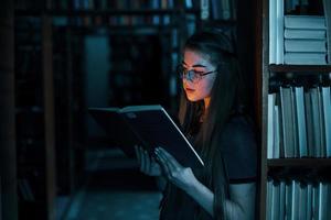 Licht aus dem Buch im dunklen Raum. Vorstellungskonzept. Studentin ist in der Bibliothek, die voller Bücher ist. Konzeption von Bildung foto