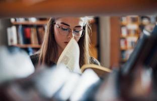 Blick durch die Regale. Studentin ist in der Bibliothek, die voller Bücher ist. Konzeption von Bildung foto