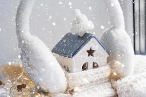 Das gemütliche Haus ist mit Mütze und Schal in ein Schneesturm-Fensterbrettdekor gehüllt. Winter, Schnee - Hausisolierung, Schutz vor Kälte und schlechtem Wetter, Raumheizung. festliche stimmung, weihnachten, neujahr foto