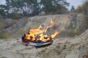 brennende sportschuhe oder turnschuhe in feuer stehen an der sandstrandküste. Sportler ausgebrannt. körperliche anstrengung während des trainingskonzepts foto