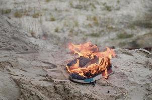 brennende sportschuhe oder turnschuhe in feuer stehen an der sandstrandküste. Sportler ausgebrannt. körperliche anstrengung während des trainingskonzepts foto