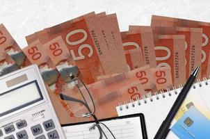 50 kanadische Dollar-Scheine und Taschenrechner mit Brille und Stift. Steuerzahlungskonzept oder Anlagelösungen. Finanzplanung oder Buchhaltungsunterlagen foto