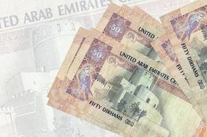 50 VAE-Dirham-Scheine liegen im Stapel auf dem Hintergrund einer großen halbtransparenten Banknote. abstrakte Darstellung der Landeswährung foto