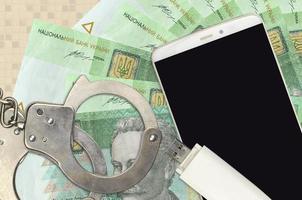 20 ukrainische Griwna-Scheine und Smartphone mit Polizeihandschellen. Konzept von Hacker-Phishing-Angriffen, illegalem Betrug oder weicher Verteilung von Malware foto