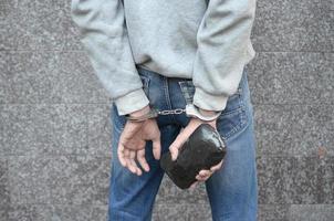 Verhafteter Drogendealer in Polizeihandschellen mit großem Heroin-Drogenpaket auf dunklem Wandhintergrund foto