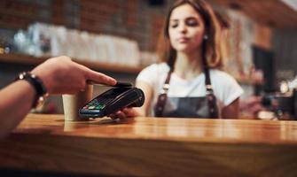 Bezahlen mit digitalem System. junge caféarbeiterin drinnen. Geschäfts- und Dienstleistungskonzept foto