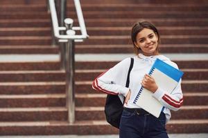 positive studentin, die tagsüber mit dokumenten im freien steht foto