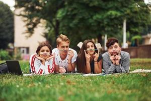 verspielte Stimmung. Gruppe junger Studenten in Freizeitkleidung auf grünem Gras tagsüber foto