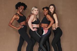 weiße und schwarze Menschen. Gruppe multiethnischer Frauen, die im Studio vor braunem Hintergrund stehen foto