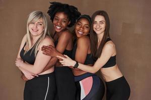 dünn und groß. Gruppe multiethnischer Frauen, die im Studio vor braunem Hintergrund stehen foto