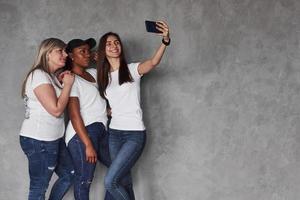 Foto für die Erinnerungen. Gruppe multiethnischer Frauen, die im Studio vor grauem Hintergrund stehen