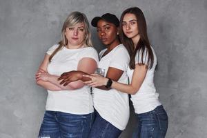 drei Personen zusammen. Gruppe multiethnischer Frauen, die im Studio vor grauem Hintergrund stehen foto