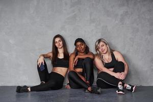 etwas Ruhe stört nicht. Gruppe multiethnischer Frauen, die im Studio vor grauem Hintergrund sitzen foto