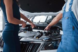 Ich denke, Ihr Problem in diesem Teil. Frau im Autosalon mit Angestellter in blauer Uniform, die ihr repariertes Auto zurücknimmt foto